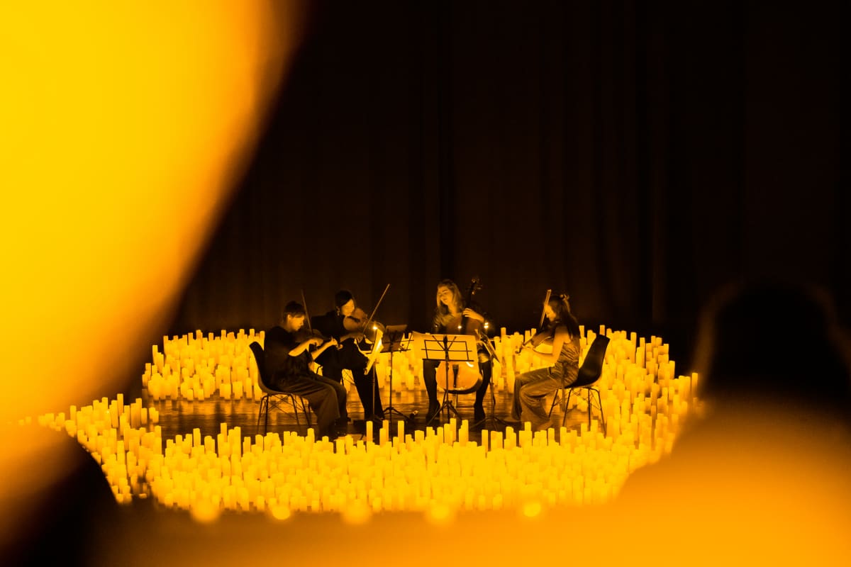 A string quartet performing on a stage bathed in the glow of candlelight.