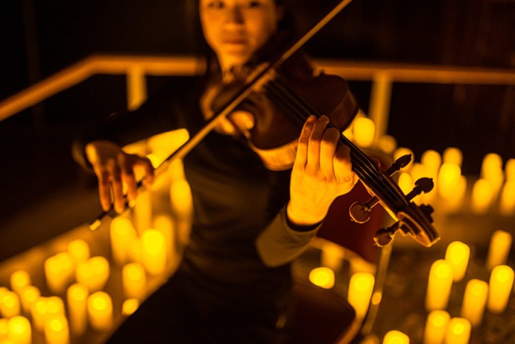 A violinist playing surrounded by hundreds of candles