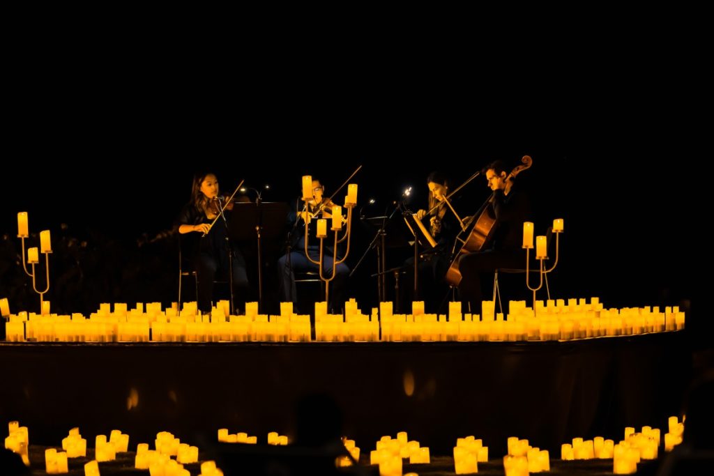 A string quartet performing on a makeshift stage surrounded by hundreds of candles