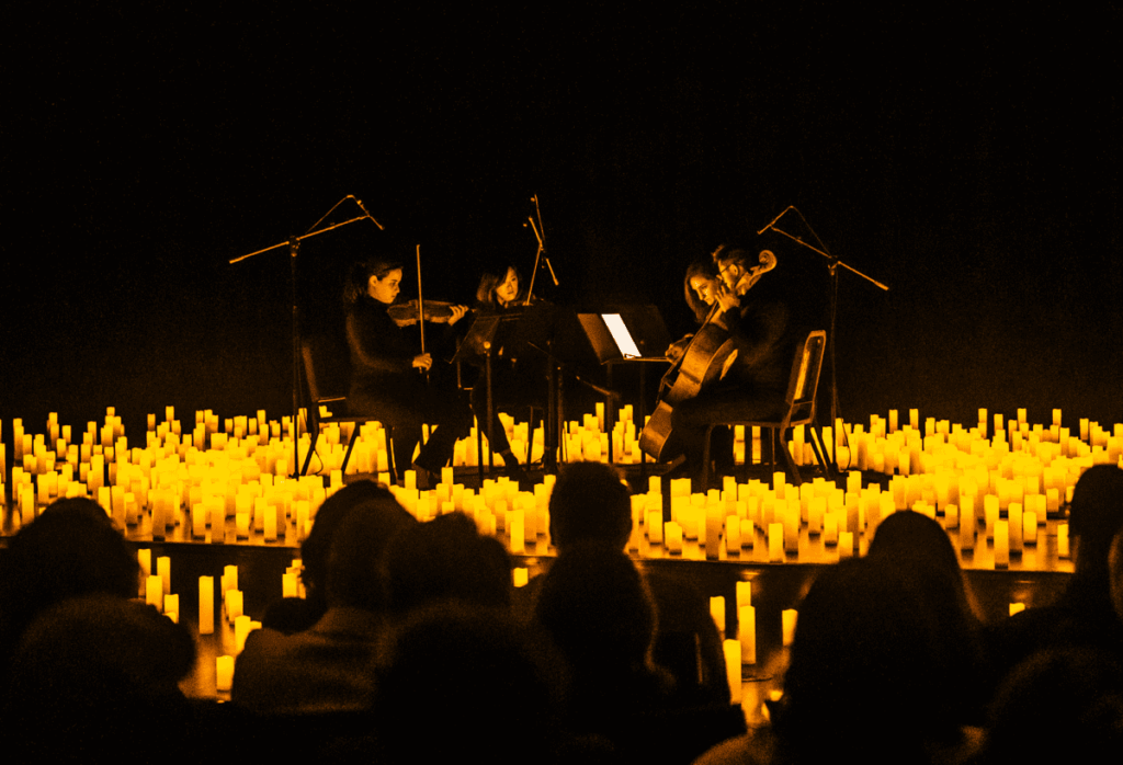 A string quartet performing on a stage covered by candles and the silhouette of the audience in the foreground.