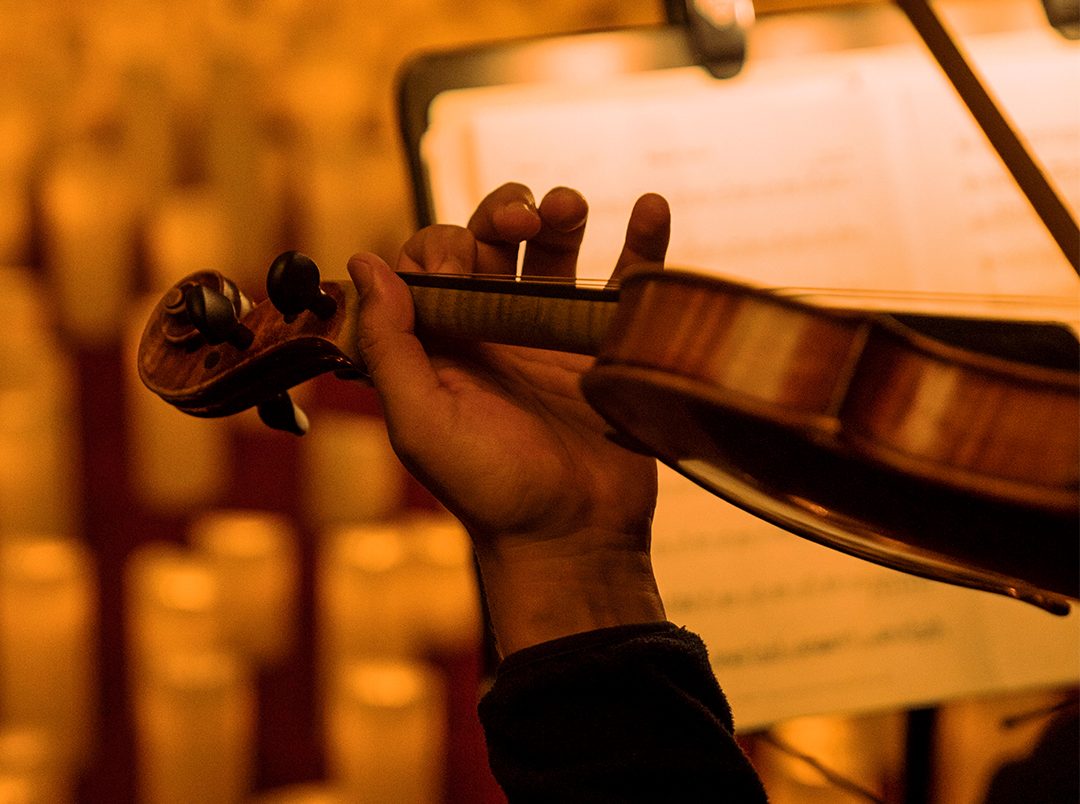 close up of person playing violin surrounded by candles