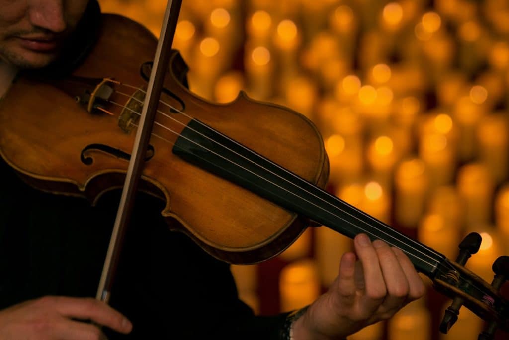 A performer plans a violin with flameless candles in the background.
