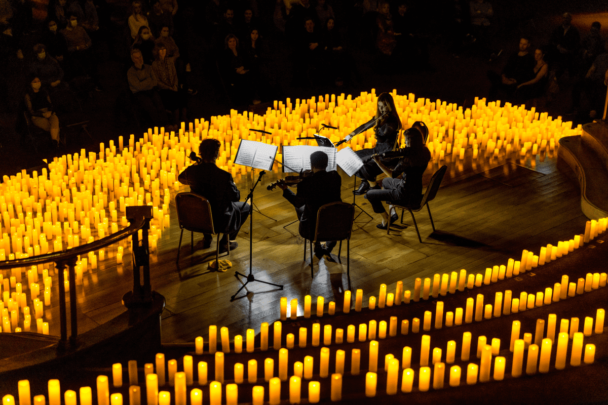 A string quartet playing on stage surrounded by a sea of candles
