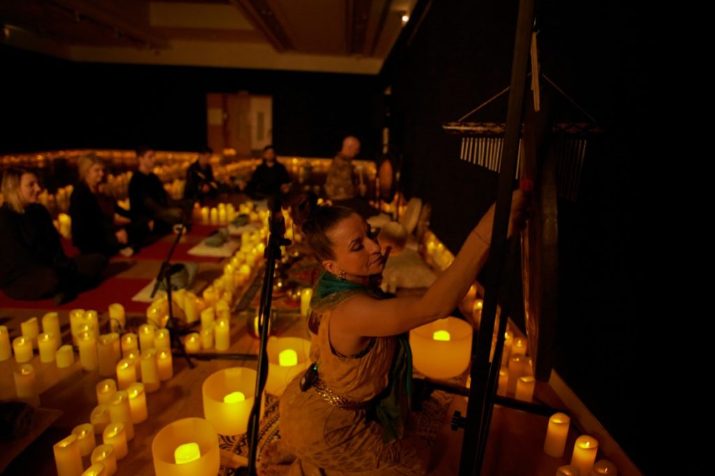 A woman playing chimes in a dimly lit room full of candles