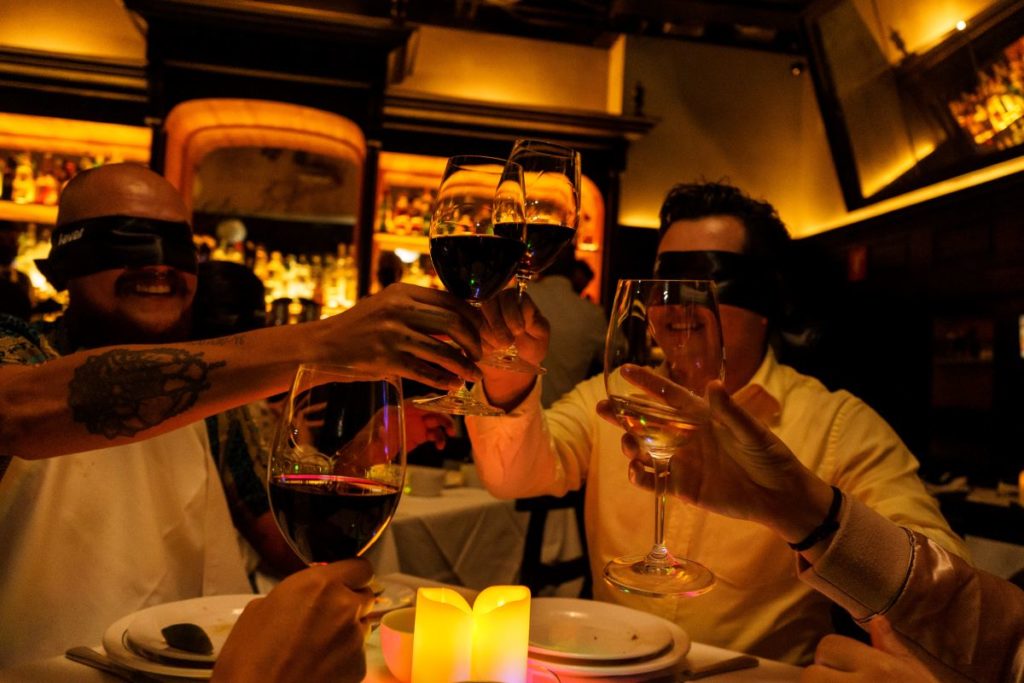 Guests clink wine glasses whilst blindfolded and surrounded by flameless candles.