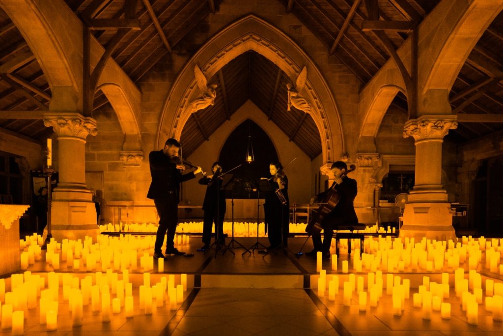 string quartet performing surrounded by candles in church attic
