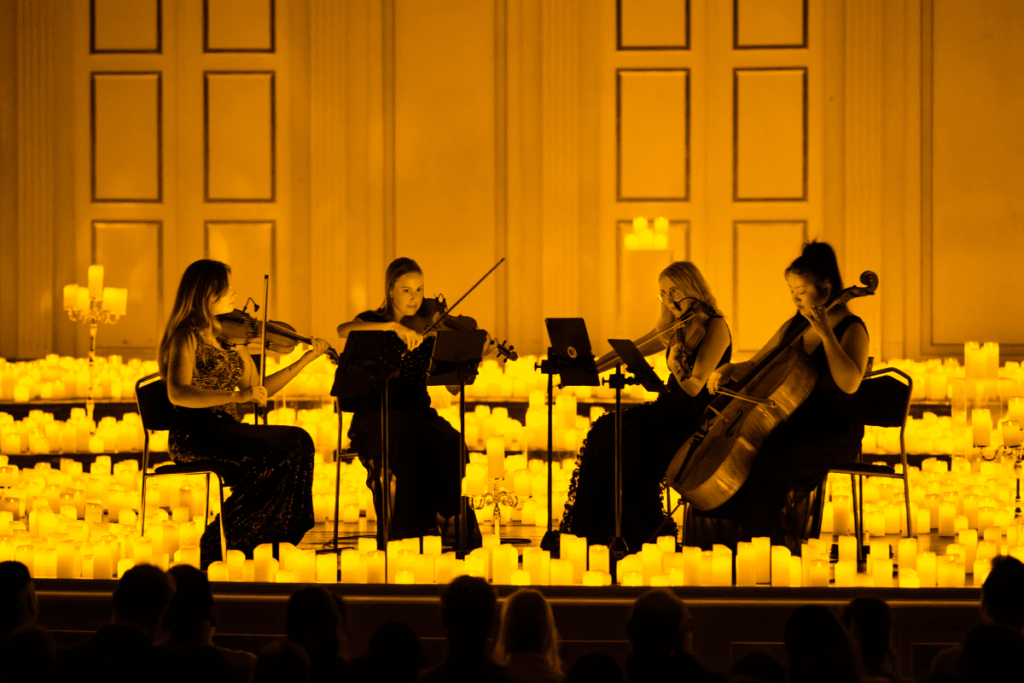 A string quartet performs on stage surrounded by candles