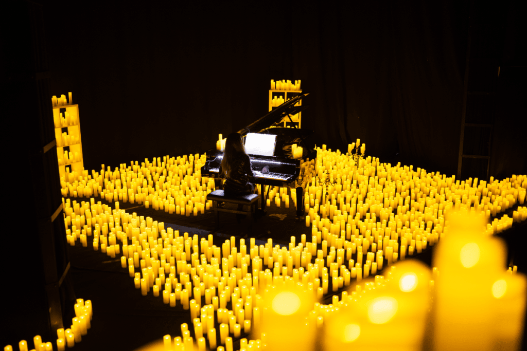 A woman sitting at and polaying the piano surrounded by candlelight.
