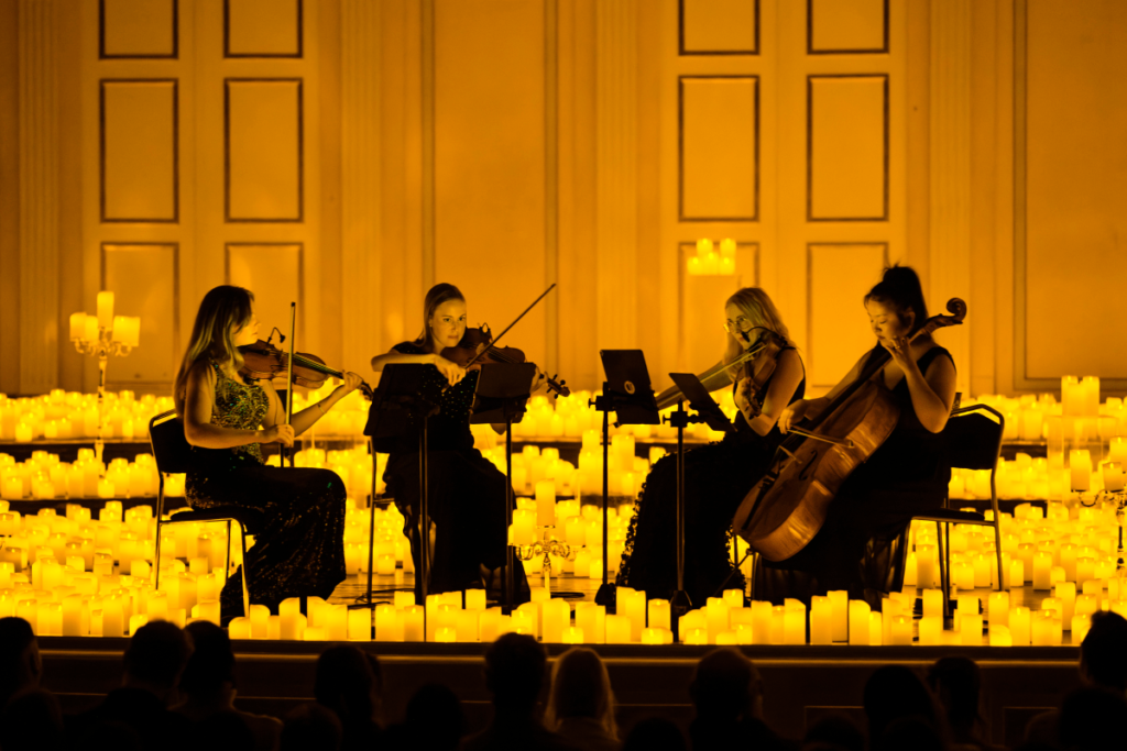 A string quartet performing on a stage surrounded by hundreds of flickering candles.