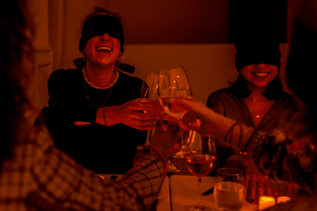 Two women smiling at a Dining in the Dark experience while making a toast