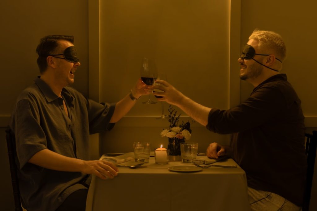 A blindfolded couple clink glasses at Dining in the Dark. 