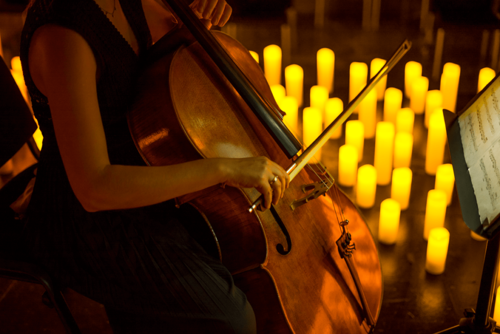 A musician playing the cello with candles in the background