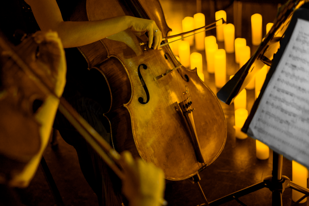 A close up of a musician playing the cello with candles in the background