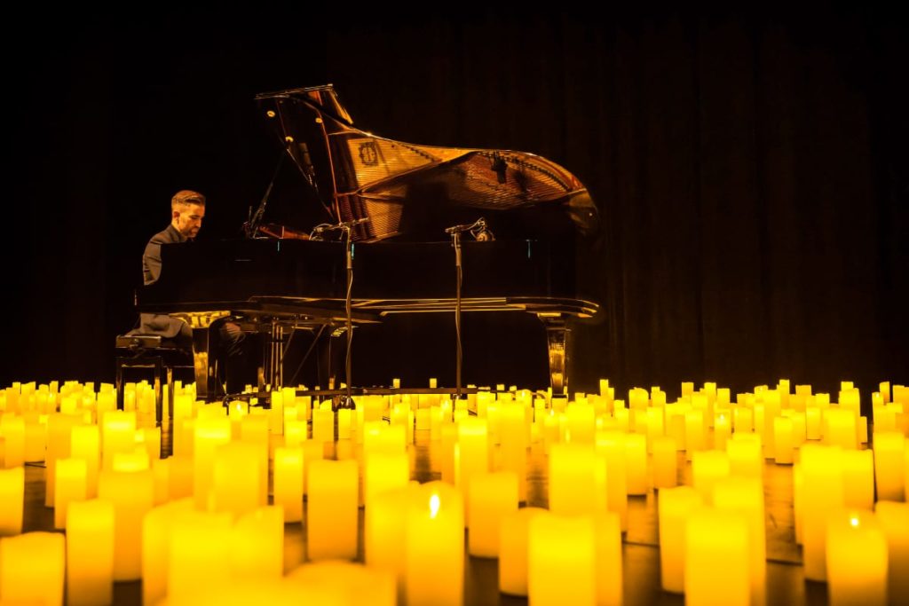 Un homme jouant du piano pour un concert Candlelight entouré de milliers de bougies