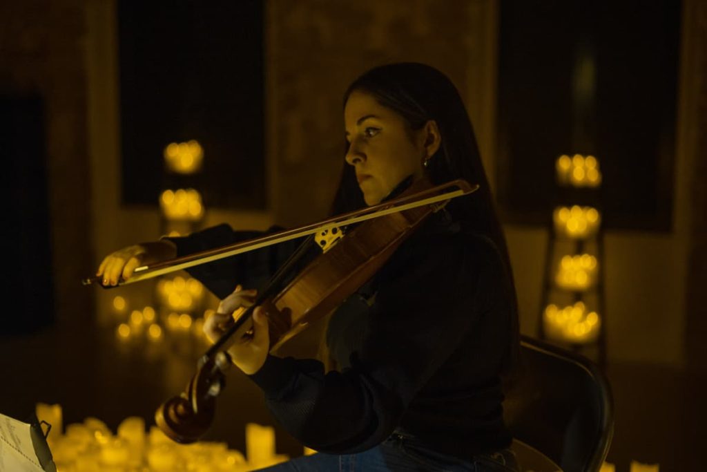 Une femme joue du violon lors d'un concert Candlelight sous la lumière des bougies