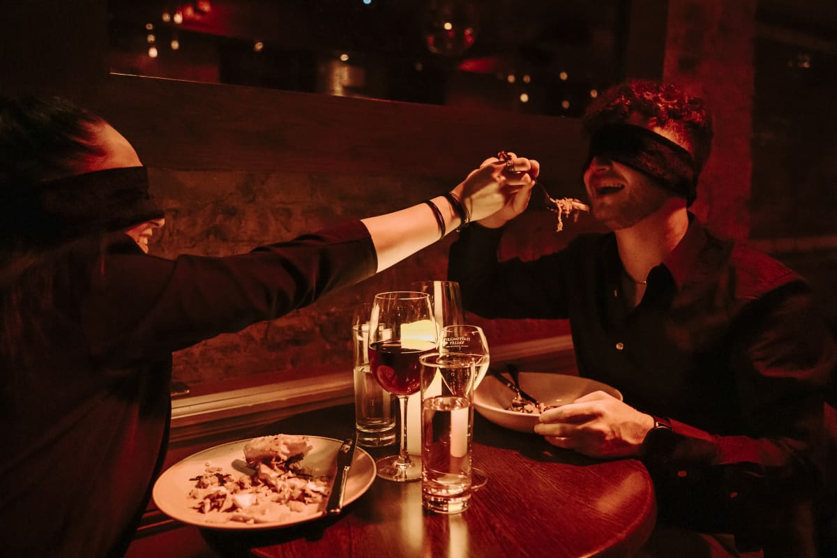 Un hombre y una mujer con los ojos vendados sentados en un restaurante a la luz de las velas en Dining in the Dark