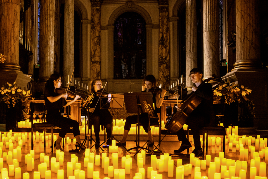 A string quartet playing on a stage filled with hundreds of candles