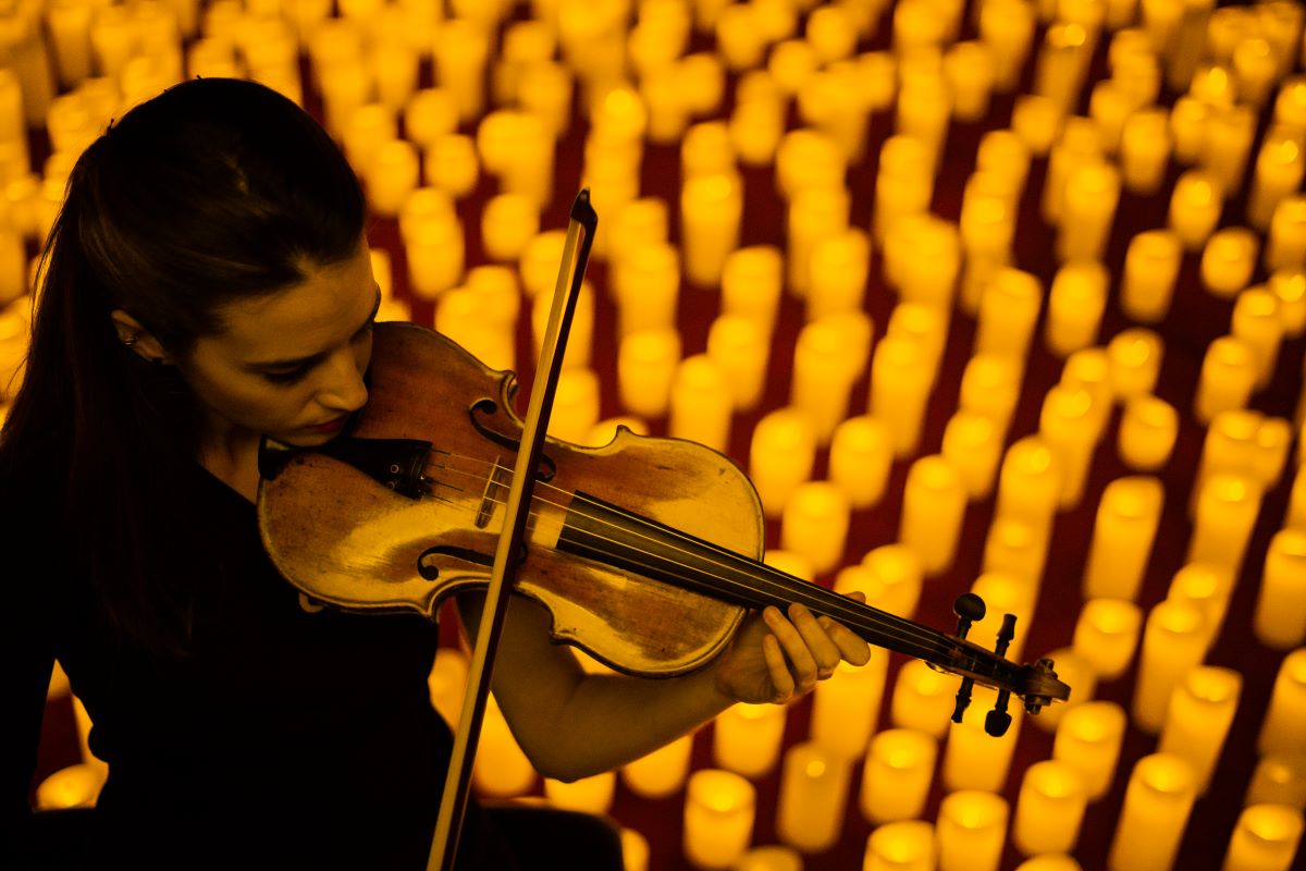 A woman playing the violin at a Taylor Swift Candlelight concert in front of a sea of candles.