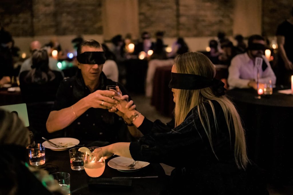 Photo d'un restaurant plei avec un couple trinquant lors d'un dîner à l'aveugle