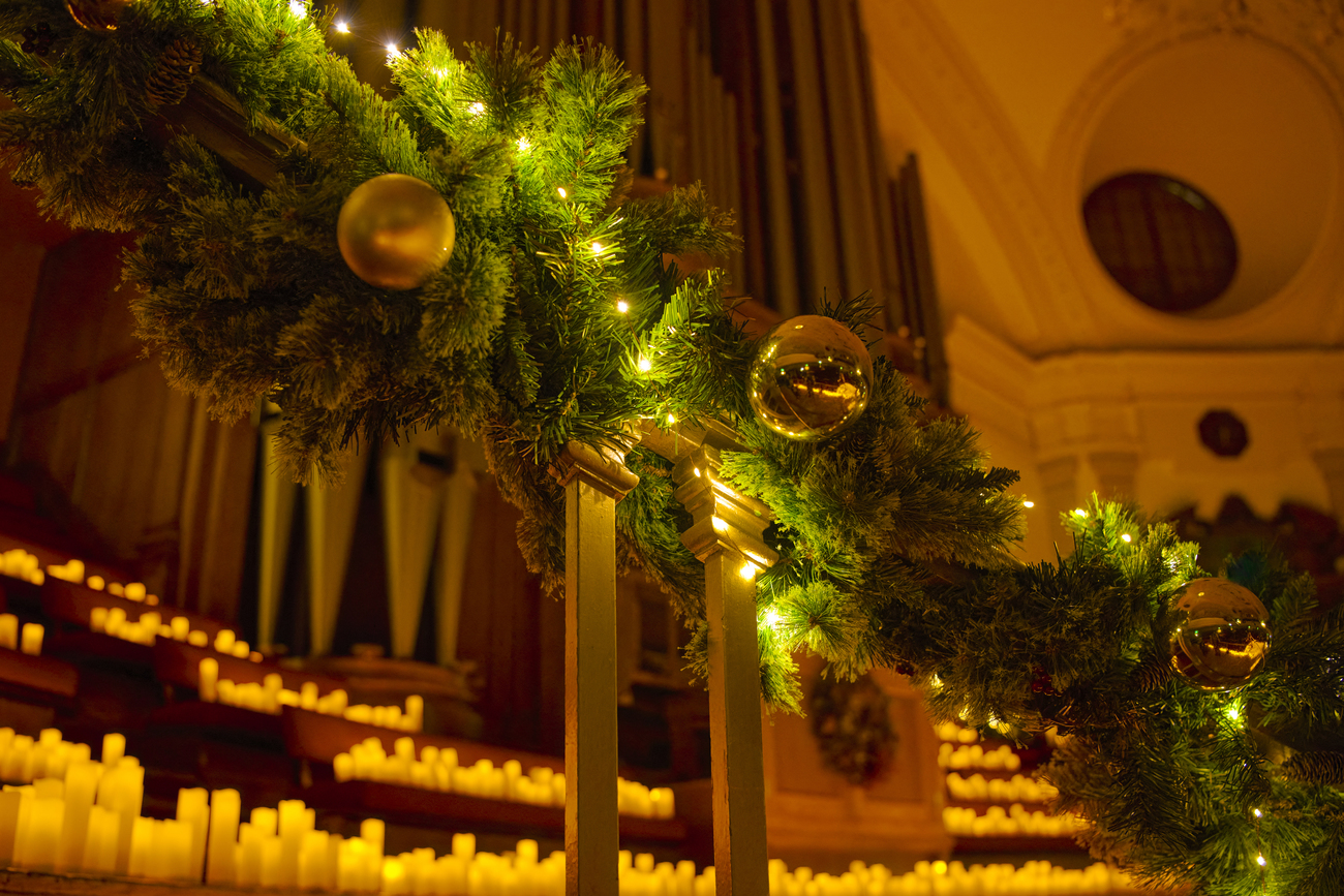 Barandilla de escaleras decorada con bolas de árbol de navidad, luces y al fondo muchas velas