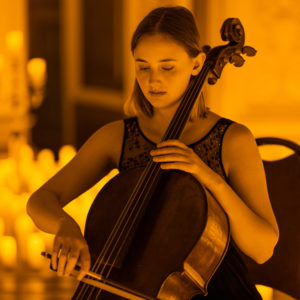 A musician plays a cello, surrounded by candlelight.