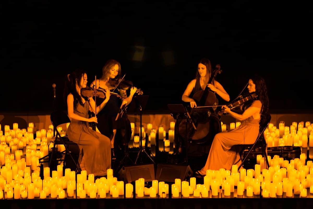 cuarteto de cuerda tocando en un escenario lleno de velas