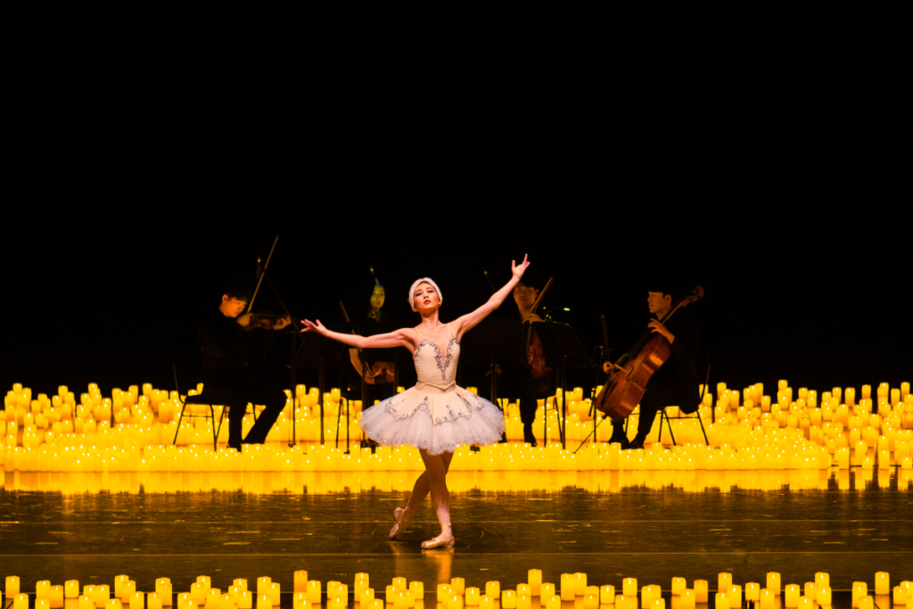 Una ballerina di danza classica che si inchina al pubblico, circondata da candele