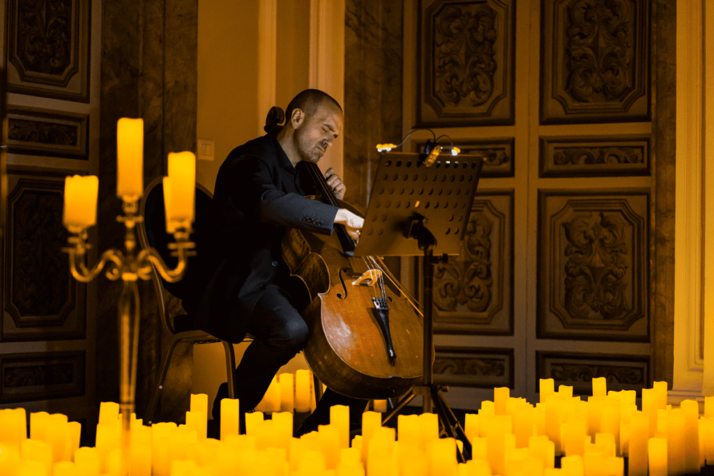 A musician playing the cello surrounded by candles