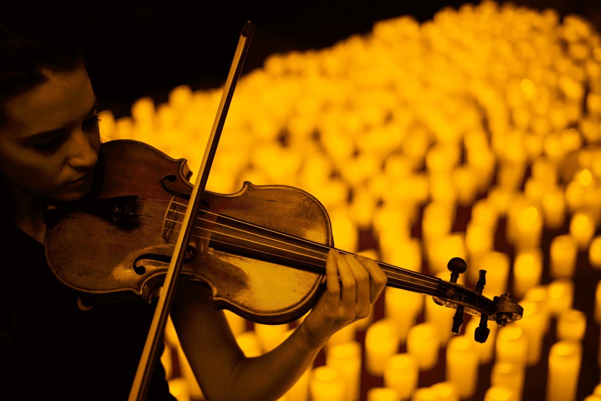 A musician playing the violin by candlelight.