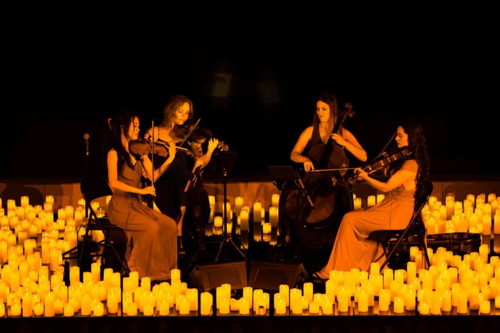 A string quartet performing on a stage, surrounded by candles.