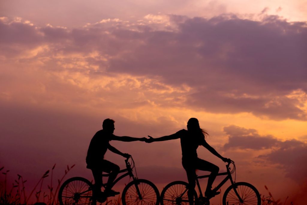 A picture of a couple cycling at sunset while holding hands.