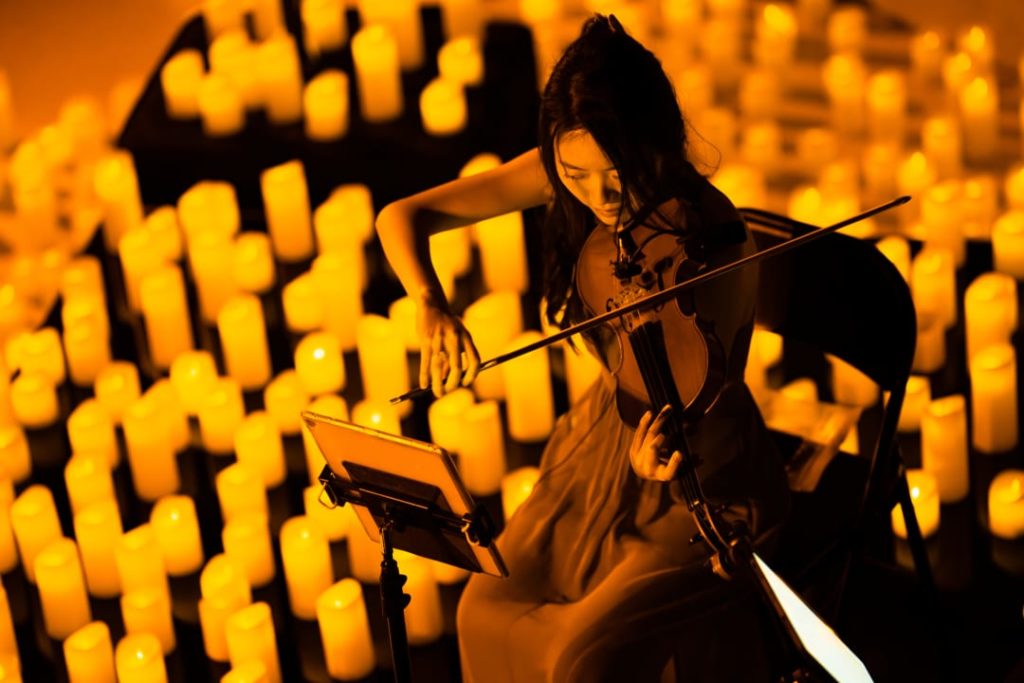 A musician playing the violin amid a sea of candles.
