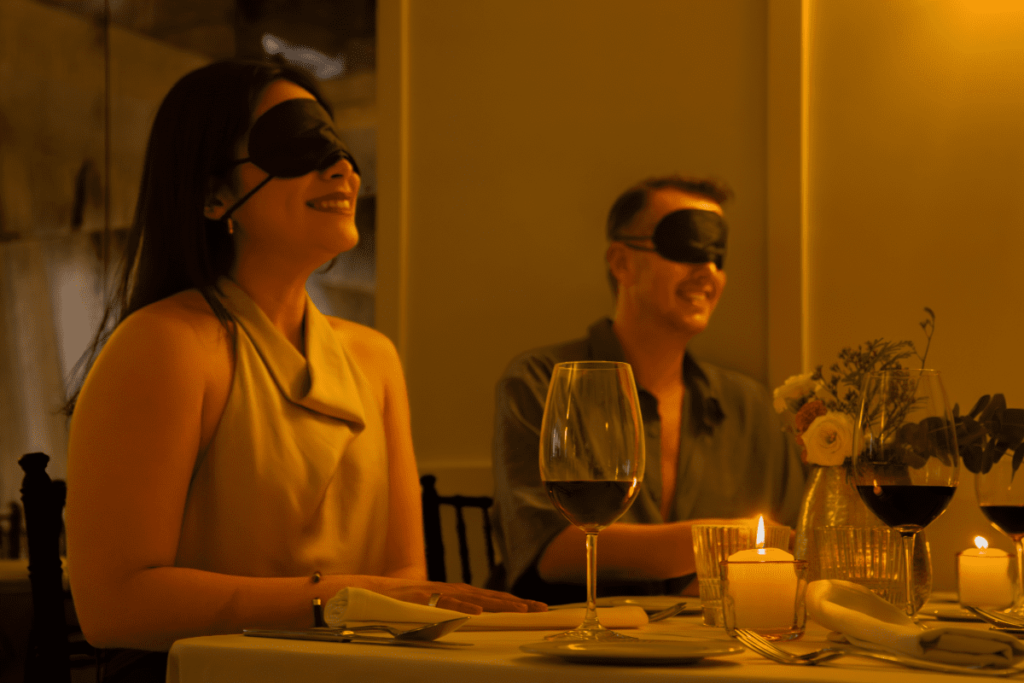 A blindfolded couple at a Dining in the Dark experience laughing