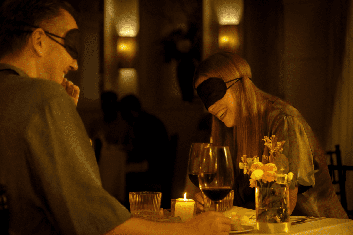 A blindfolded couple laughing at a Dining in the Dark dinner