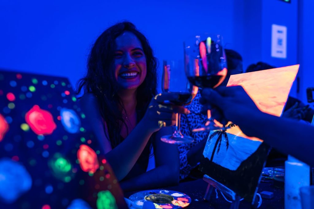 A woman clinking red wine glasses at Neon Brush.