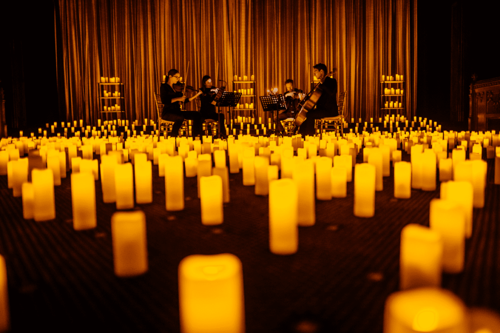 string quartet performing on stage in front of a curtain while thousands of candles flicker around them