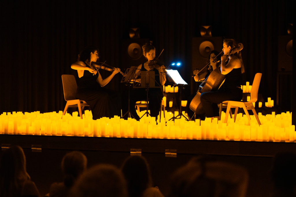 A string quartet performing on stage amid a sea of candles