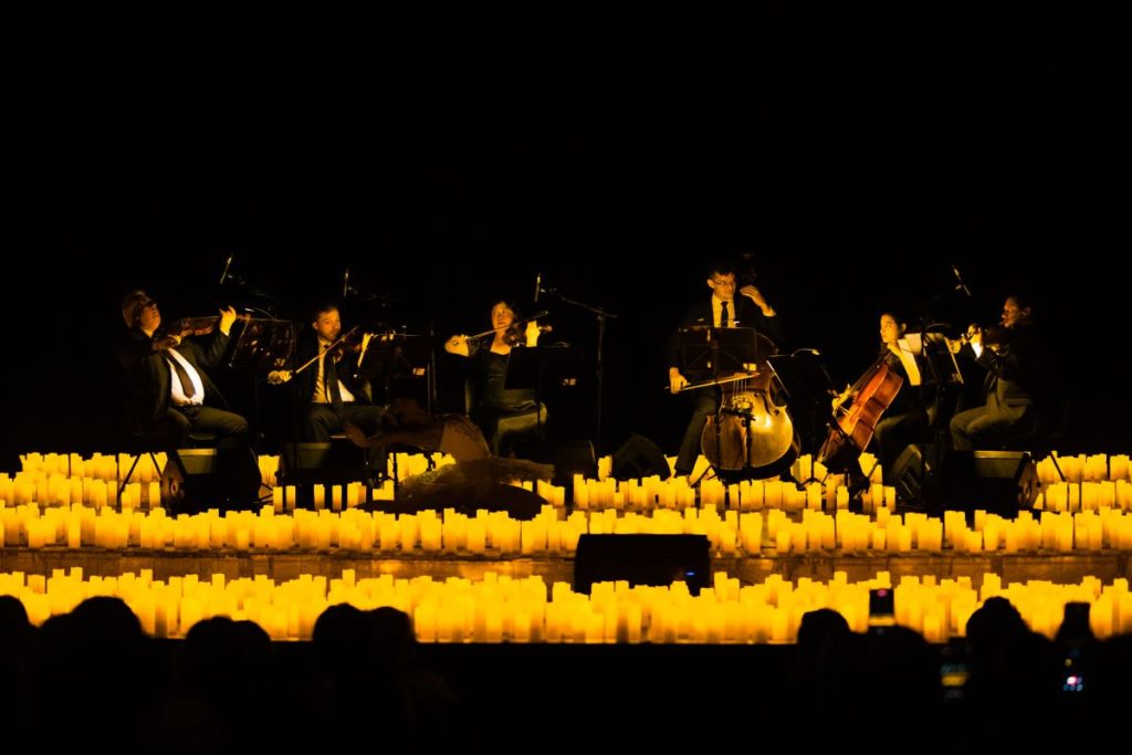 Um sexteto de cordas apresentando um concerto Candlelight em um palco cercado por luz de velas.