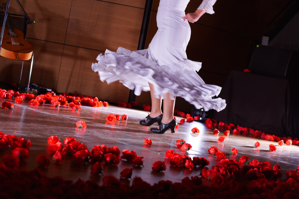 A flamenco dancer in a white dress performing at We Call It Flamenco